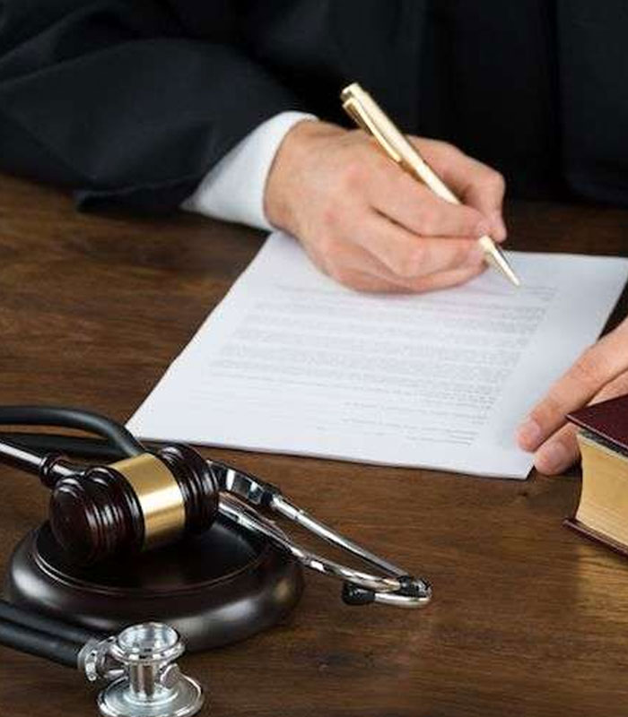 Attorney writes in a trial document. Near attorney, there is a law book, stethoscope and law hammer